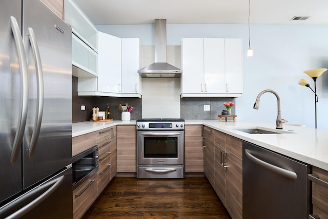 kitchen with stainless steel appliances, wall chimney exhaust hood, a sink, light countertops, and dark wood-type flooring