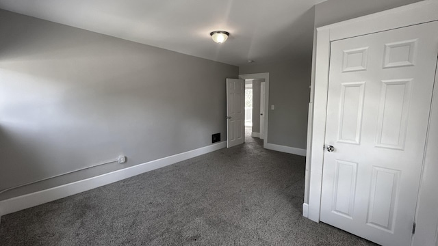 unfurnished room featuring baseboards and dark colored carpet