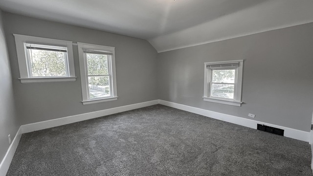 empty room featuring vaulted ceiling, dark carpet, and baseboards