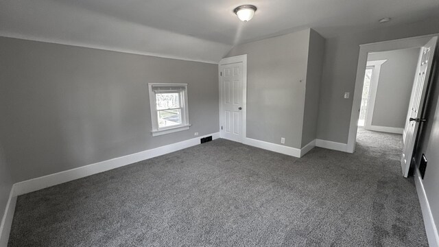 spare room featuring dark colored carpet, baseboards, and vaulted ceiling