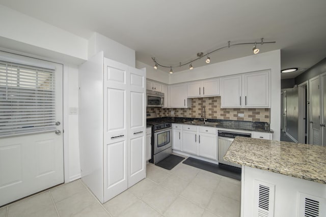 kitchen featuring appliances with stainless steel finishes, a sink, white cabinets, light tile patterned floors, and backsplash
