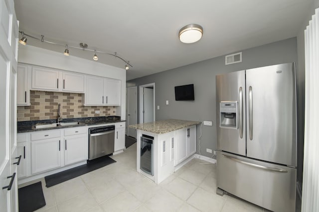 kitchen with stainless steel appliances, a sink, decorative backsplash, white cabinetry, and dark stone counters