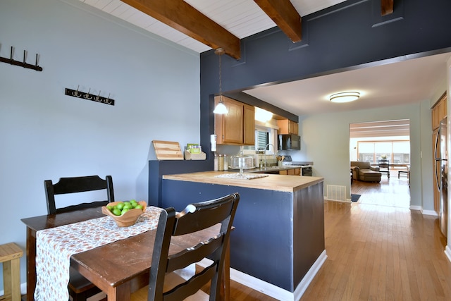 kitchen featuring black microwave, light countertops, beam ceiling, light wood-type flooring, and a peninsula