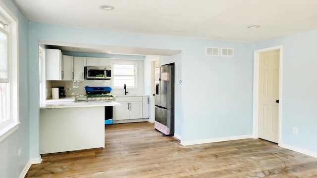 kitchen featuring appliances with stainless steel finishes, light countertops, a sink, white cabinets, and light wood-style floors