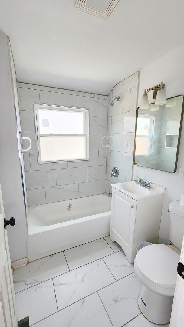 full bathroom with marble look tiles, bathtub / shower combination, vanity, and toilet