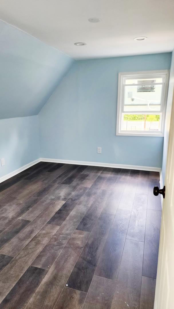 additional living space with dark wood-type flooring, vaulted ceiling, and baseboards