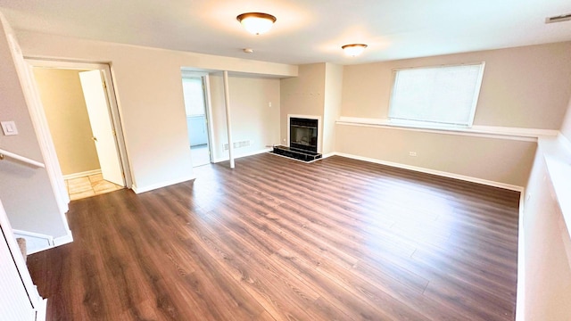 unfurnished living room with wood finished floors, a glass covered fireplace, baseboards, and plenty of natural light