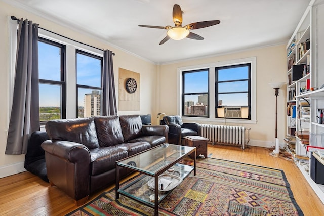 living room featuring radiator heating unit, wood-type flooring, a ceiling fan, crown molding, and baseboards