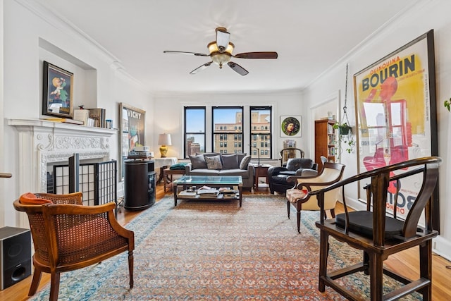 living area with wood finished floors, ceiling fan, ornamental molding, and a fireplace