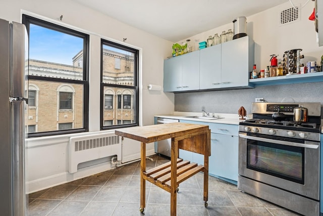 kitchen with stainless steel appliances, radiator heating unit, light countertops, tile patterned floors, and a sink