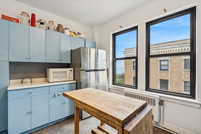 kitchen featuring white microwave, radiator, freestanding refrigerator, and blue cabinetry