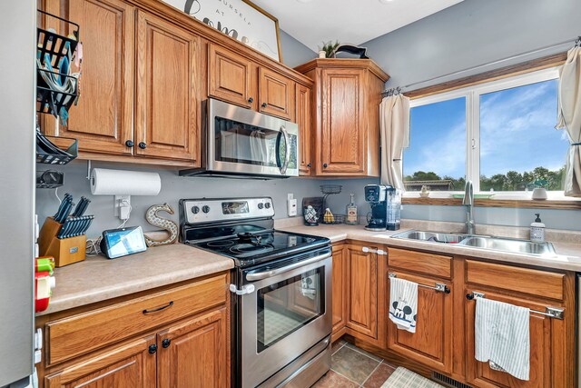 kitchen with stainless steel appliances, a sink, brown cabinets, and light countertops