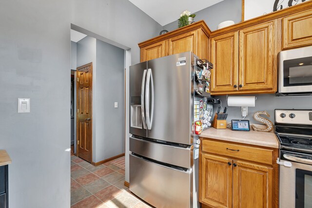 kitchen with appliances with stainless steel finishes, light countertops, brown cabinetry, and baseboards