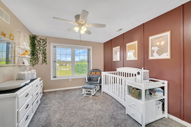 carpeted bedroom featuring baseboards, ceiling fan, and a crib
