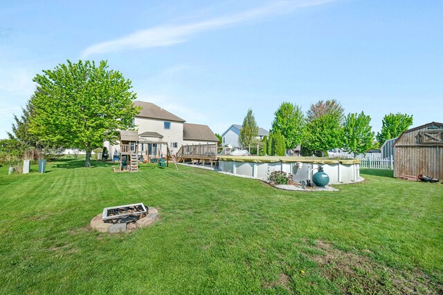 view of green lawn with a fire pit, a playground, and an outbuilding