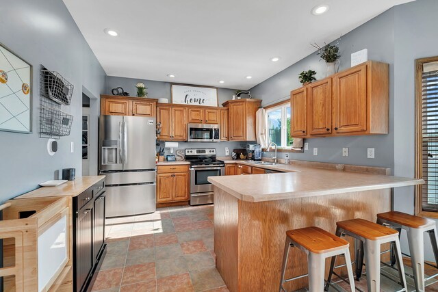 kitchen featuring appliances with stainless steel finishes, a peninsula, light countertops, a kitchen bar, and recessed lighting
