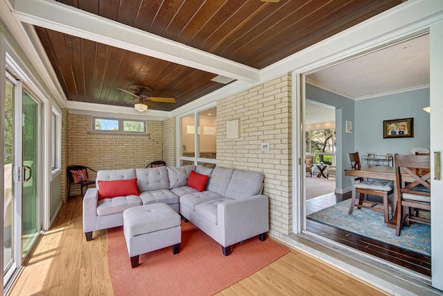 living room featuring brick wall, light wood-type flooring, ceiling fan, wooden ceiling, and ornamental molding