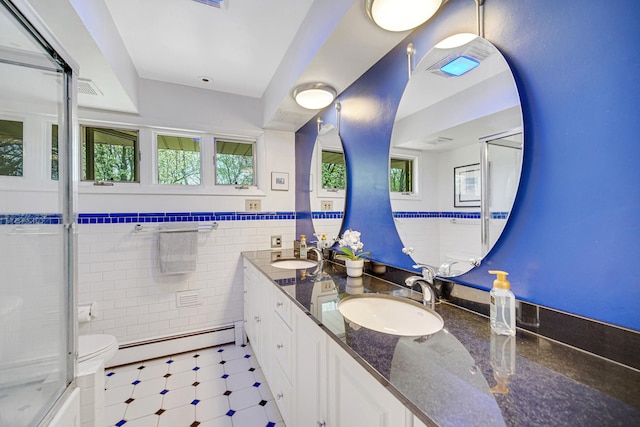 full bath featuring baseboard heating, plenty of natural light, wainscoting, double vanity, and a shower with door