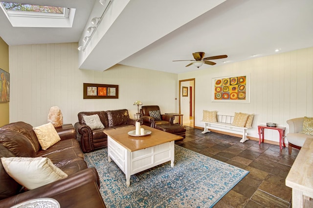living area featuring stone tile floors, ceiling fan, wood walls, a skylight, and baseboards