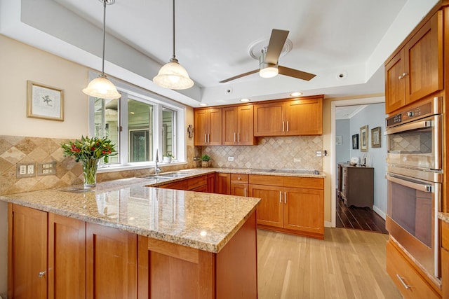 kitchen featuring double oven, a peninsula, brown cabinetry, a sink, and light wood-type flooring