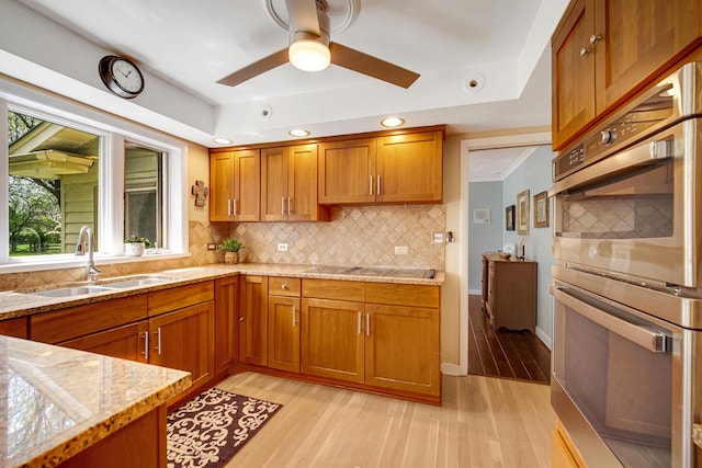 kitchen featuring a sink, stainless steel double oven, brown cabinetry, light wood-type flooring, and recessed lighting