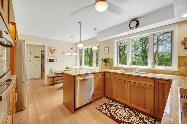 kitchen with a sink, appliances with stainless steel finishes, light stone countertops, brown cabinets, and a peninsula