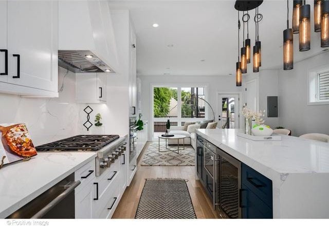 kitchen with stainless steel appliances, wall chimney range hood, light wood-type flooring, open floor plan, and white cabinets