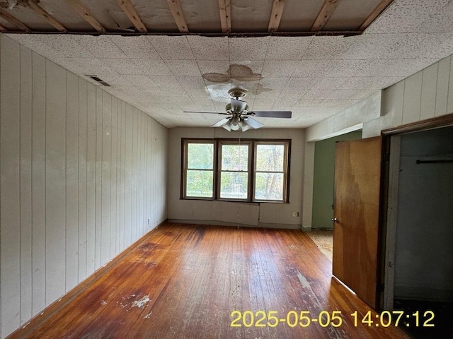 interior space featuring a paneled ceiling, ceiling fan, hardwood / wood-style flooring, and wooden walls