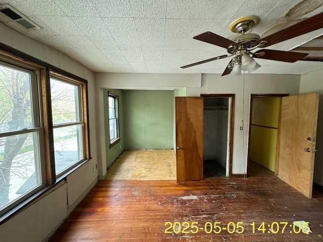unfurnished bedroom with multiple closets, hardwood / wood-style flooring, a ceiling fan, and visible vents