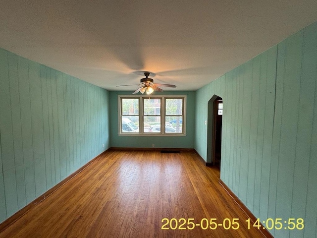 empty room with arched walkways, wooden walls, ceiling fan, and wood finished floors