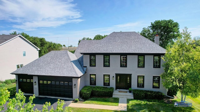 colonial home with roof with shingles, a front yard, and an attached garage