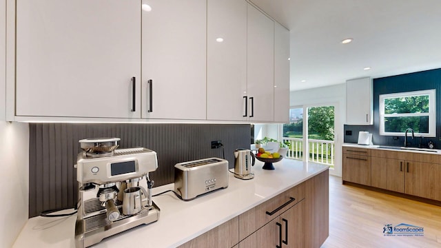 kitchen with a sink, light countertops, decorative backsplash, light wood-style flooring, and modern cabinets