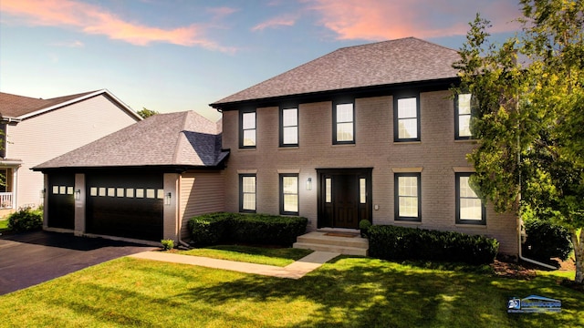 colonial inspired home with roof with shingles, a front lawn, a garage, and driveway
