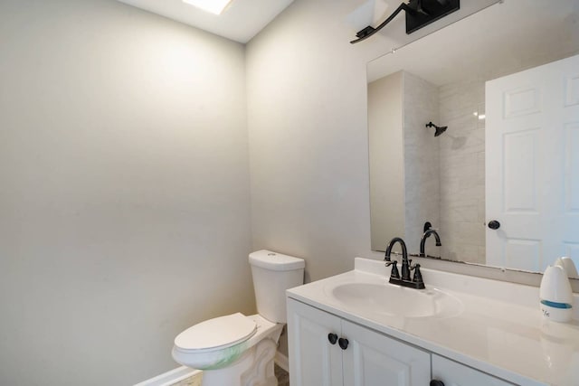 full bathroom with toilet, a tile shower, vanity, and baseboards