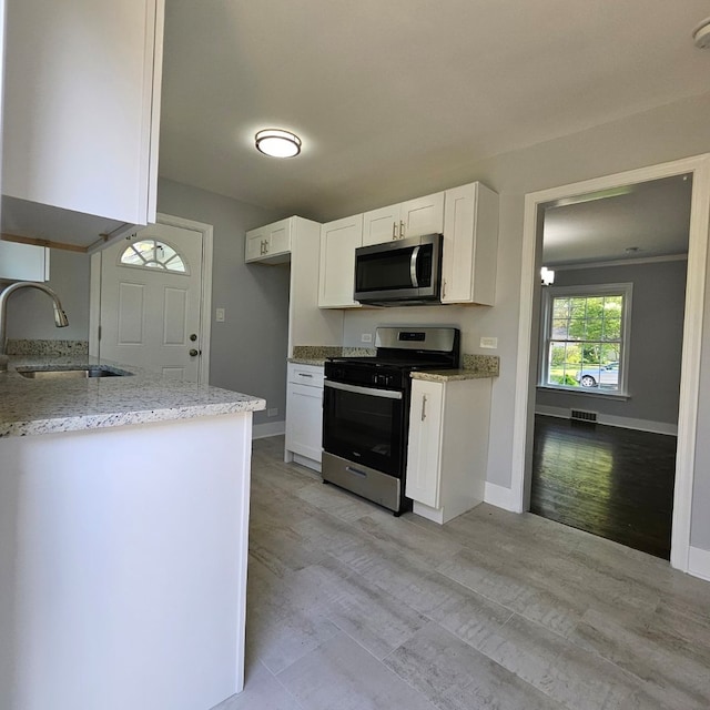 kitchen with appliances with stainless steel finishes, a sink, white cabinetry, light stone counters, and baseboards