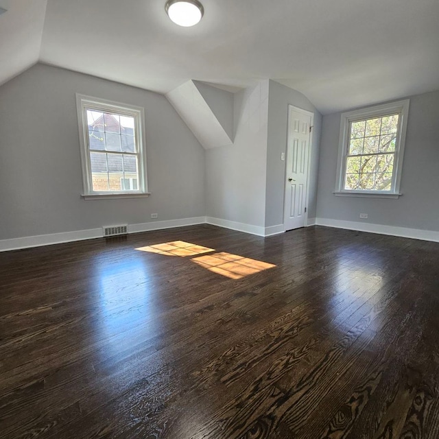 additional living space with lofted ceiling, dark wood-style floors, healthy amount of natural light, and baseboards