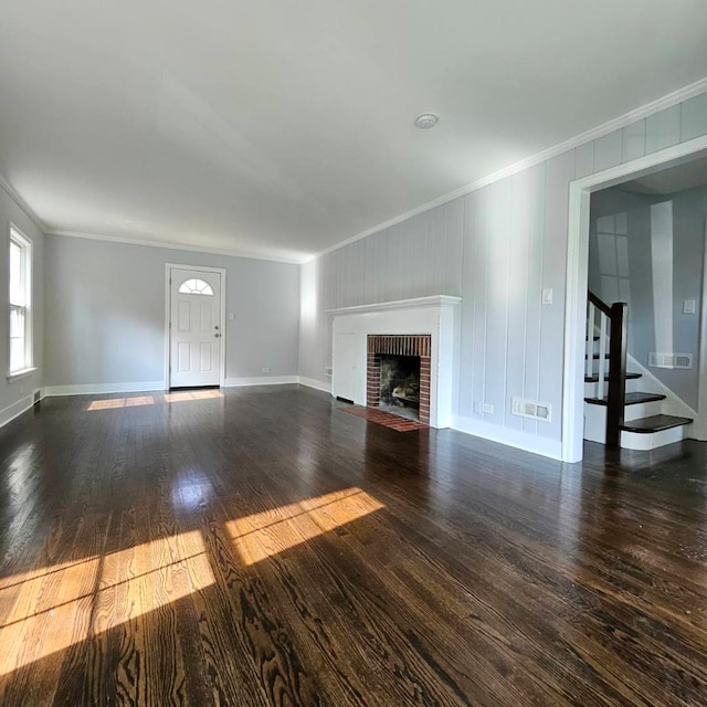 unfurnished living room featuring crown molding, stairs, hardwood / wood-style flooring, a brick fireplace, and baseboards