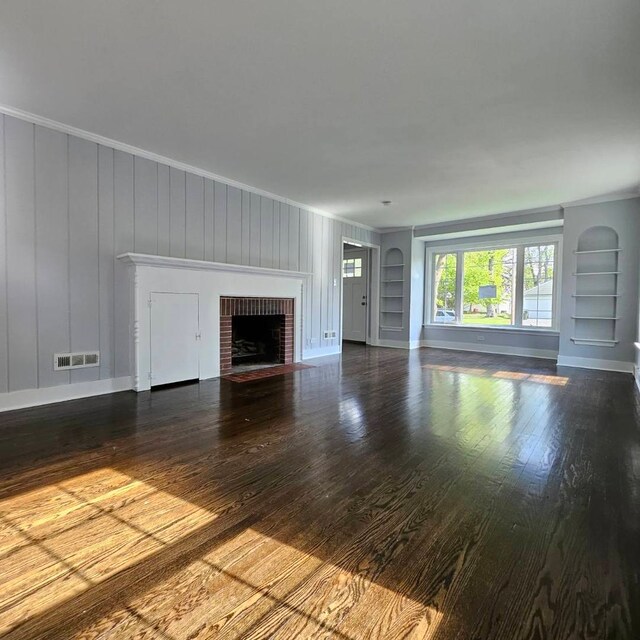 unfurnished living room featuring built in shelves, a fireplace, wood finished floors, baseboards, and crown molding