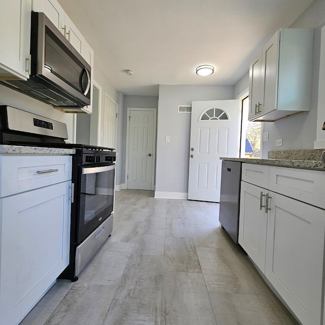 kitchen featuring appliances with stainless steel finishes, light stone counters, white cabinetry, and baseboards