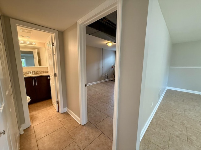 corridor with light tile patterned flooring, baseboards, and a sink
