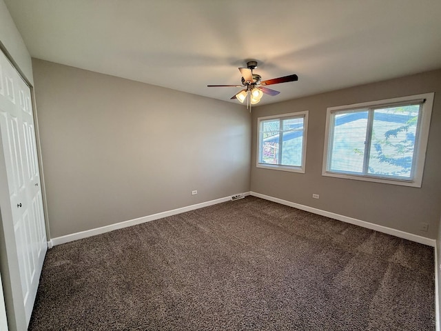 unfurnished bedroom featuring a closet, dark colored carpet, baseboards, and a ceiling fan