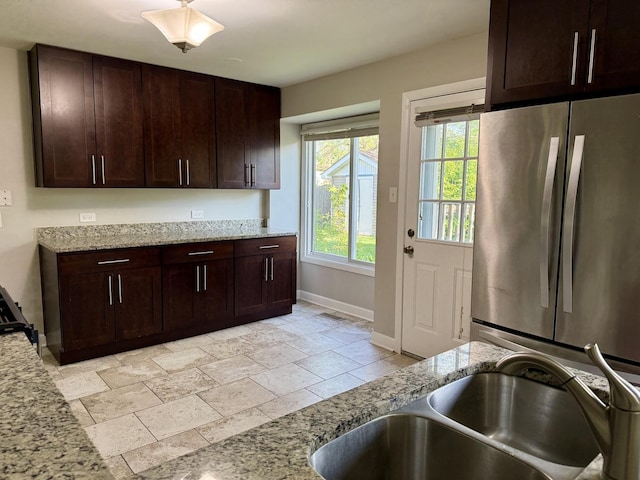 kitchen featuring freestanding refrigerator, baseboards, stone tile floors, and light stone counters
