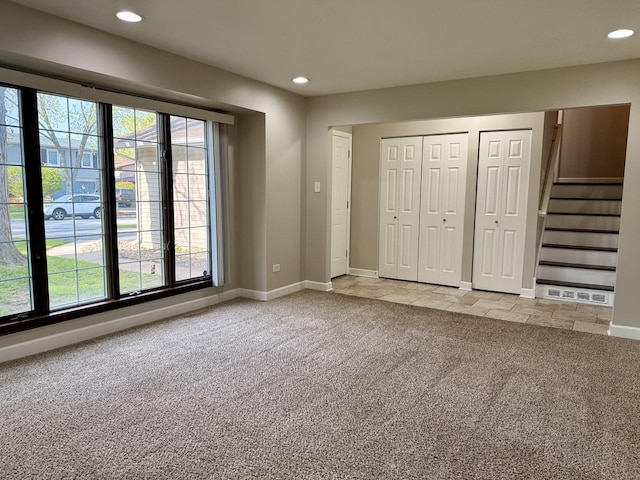 unfurnished bedroom featuring light colored carpet, multiple closets, recessed lighting, multiple windows, and baseboards