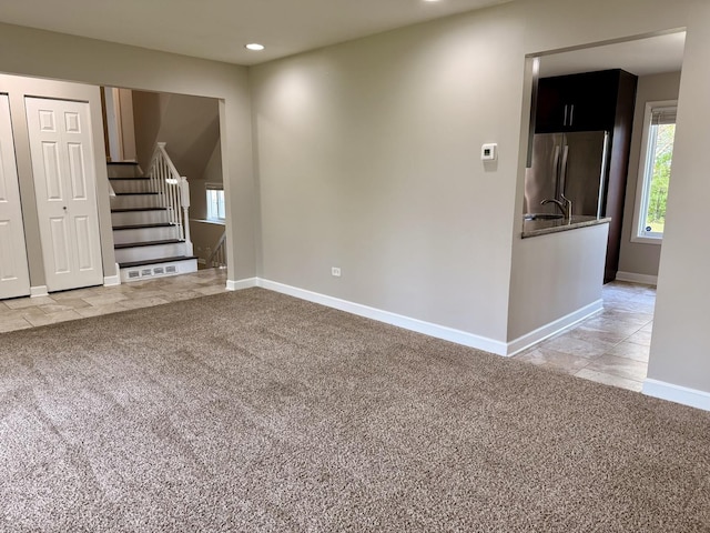 unfurnished living room featuring light colored carpet, stairway, baseboards, recessed lighting, and plenty of natural light