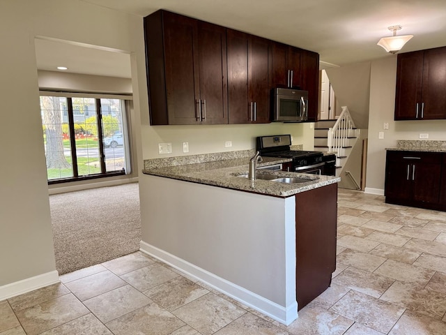 kitchen featuring stainless steel appliances, light stone counters, a sink, dark brown cabinets, and baseboards