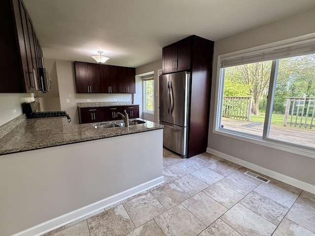 kitchen featuring stainless steel appliances, a sink, baseboards, stone countertops, and dark brown cabinetry