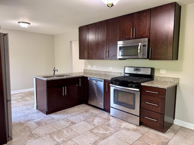 kitchen featuring stainless steel appliances, a sink, a peninsula, baseboards, and light stone countertops
