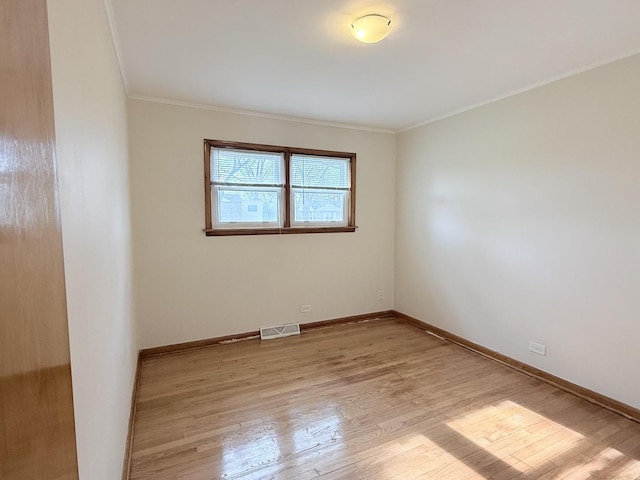 spare room featuring crown molding, light wood-type flooring, and baseboards