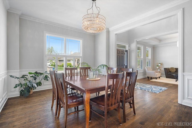 dining space with healthy amount of natural light, crown molding, dark wood-style flooring, a wainscoted wall, and a chandelier