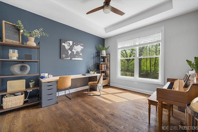 office featuring wood finished floors, a ceiling fan, a tray ceiling, and baseboards